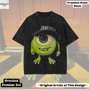 K&ouml;nnte beinhalten: Schwarzes, &uuml;bergro&szlig;es Premium-T-Shirt mit einer Cartoonfigur mit einem Auge, die einen Hut mit "MIU" tr&auml;gt. Die Figur ist gr&uuml;n mit einem gro&szlig;en Auge und einem l&auml;chelnden Mund. Das Shirt hat den Text "Premium Wash: Black" und "Oversized Premium Tee!"