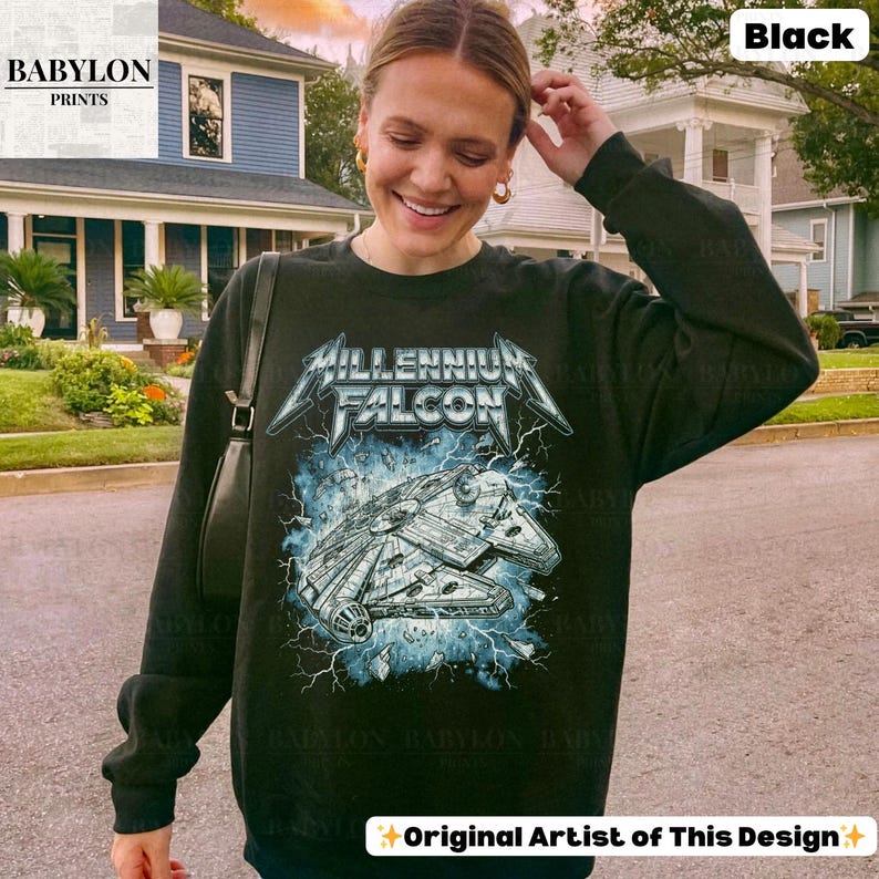 May include: Black sweatshirt featuring a graphic of the Millennium Falcon spaceship with the text "Millennium Falcon" in a stylized font. The design includes blue lightning effects. The sweatshirt is from Babylon Prints.