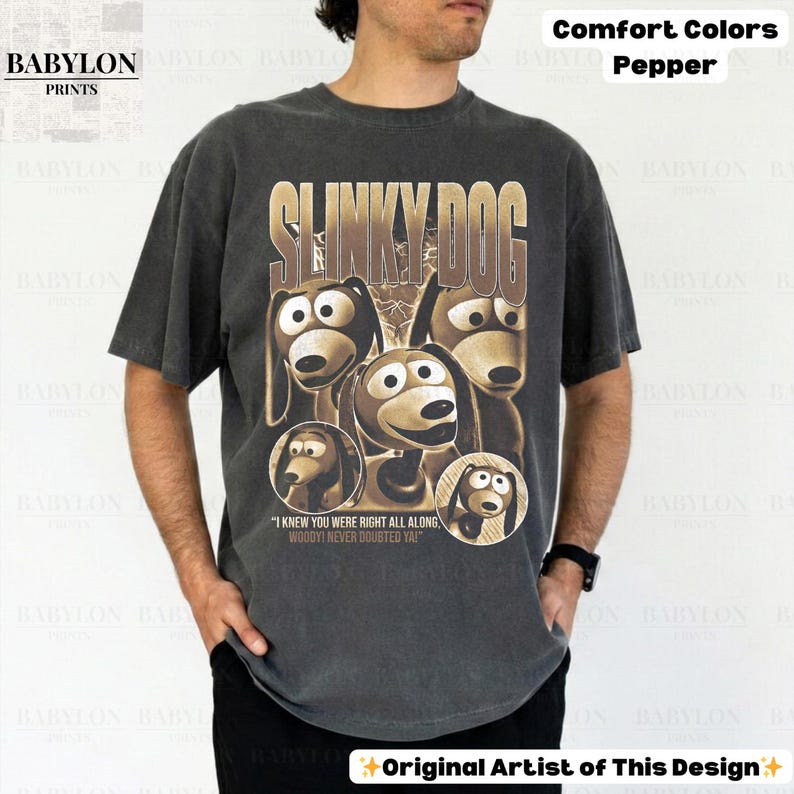 May include: A dark gray t-shirt featuring a graphic of Slinky Dog from Toy Story. The design includes the text "SLINKY DOG" and the quote "I KNEW YOU WERE RIGHT ALL ALONG WOODY! NEVER DOUBTED YA!" The shirt is labeled "Comfort Colors Pepper."