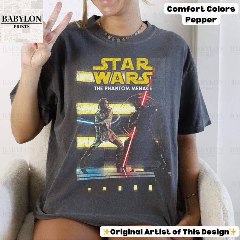 Puede incluir: Camiseta gris oscuro con un gr&aacute;fico de Star Wars. El dise&ntilde;o incluye el texto "STAR WARS THE PHANTOM MENACE" e ilustraciones de personajes con sables de luz. La camiseta est&aacute; etiquetada como "Comfort Colors Pepper".