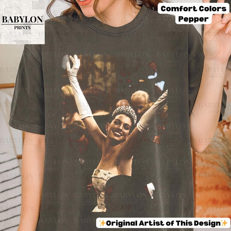 May include: A Comfort Colors pepper-coloured t-shirt with a vintage image of a woman in a gown, gloves, and tiara, arms raised. The shirt features the text "BABYLON PRINTS" and "Original Artist of This Design".
