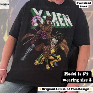 May include: Black oversized t-shirt featuring a graphic of X-Men characters Gambit and Rogue. The X-MEN text is in white and green. The shirt has the text "Original Artist of This Design".