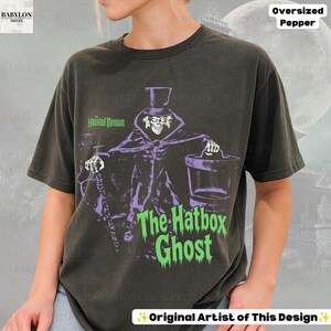 Puede incluir: Una camiseta gris carb&oacute;n de manga corta con un gr&aacute;fico de The Hatbox Ghost de The Haunted Mansion. El dise&ntilde;o muestra al personaje con sombrero de copa, bast&oacute;n y sombrerera, junto con el texto The Haunted Mansion y The Hatbox Ghost.