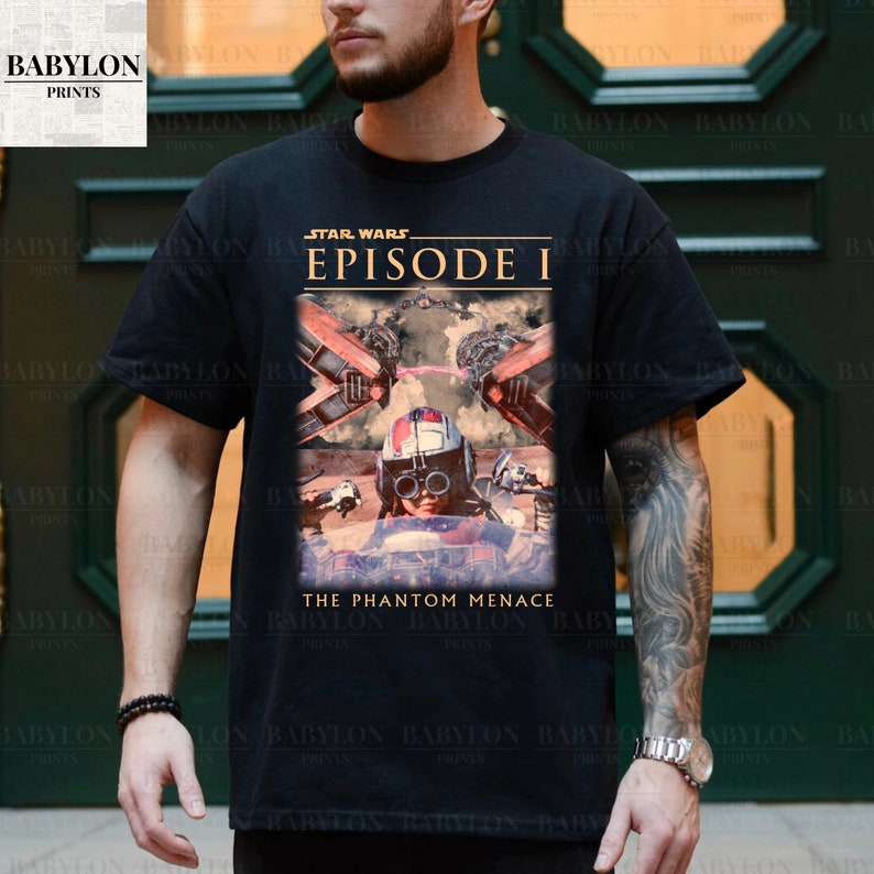Op de afbeelding: Zwart T-shirt met een afbeelding van Star Wars: Episode I - The Phantom Menace. Het ontwerp bevat de filmtitel en een afbeelding van een personage in een cockpit. Het Babylon Prints-logo staat linksboven.
