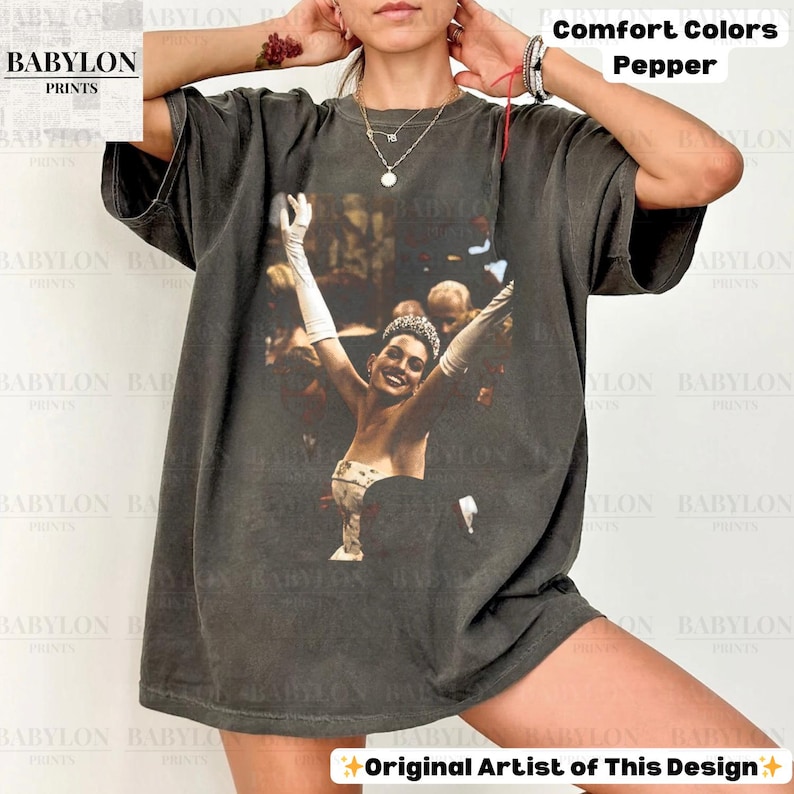 May include: Dark grey Comfort Colors t-shirt with a graphic of a woman wearing a tiara and gloves, arms raised. The shirt has the text "Original Artist of This Design" and "Comfort Colors Pepper".