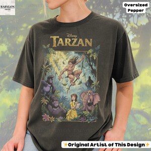 May include: Dark gray oversized t-shirt featuring a colorful graphic from Disney's Tarzan. The design includes Tarzan, gorillas, Jane, and an elephant. The shirt has the text "Disney Tarzan", "Oversized Pepper", and "Original Artist of This Design".