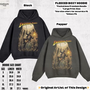 May include: Black and pepper-colored fleeced boxy hoodies featuring the Indiana Jones logo and graphic. The hoodies have a large print size and are unisex fit. A size chart is included. The design is by the original artist.