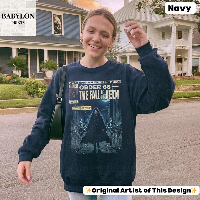 May include: Navy blue sweatshirt featuring a Star Wars comic book cover design. The graphic includes the text "STAR WARS - ORDER 66 - THE FALL OF THE JEDI" with illustrations of characters and scenes from the movie. The sweatshirt has long sleeves.