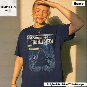 May include: Navy blue t-shirt featuring a comic book-style graphic from Star Wars. The graphic reads "Order 66: The Fall of the Jedi" with illustrations of characters and text. The shirt has short sleeves and a crew neck.