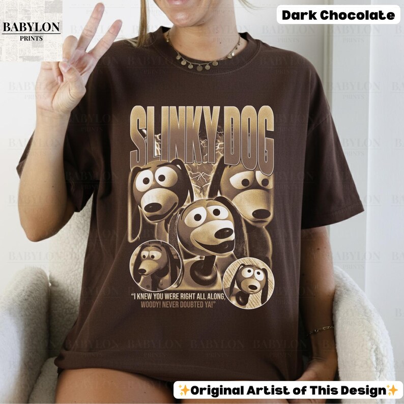 May include: Dark chocolate-colored t-shirt featuring a graphic of Slinky Dog from Toy Story. The design includes the text "SLINKY DOG" in a gold font, along with images of the character. The shirt also has the quote "I KNEW YOU WERE RIGHT ALL ALONG, WOODY! NEVER DOUBTED YA!"