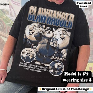 May include: Black oversized t-shirt featuring Clawhauser from Zootopia. The graphic includes Clawhauser and the text "CLAWHAUSER" in blue and white. Additional text includes "ZOOTOPIA" and quotes about Gazelle. The shirt is a size S.