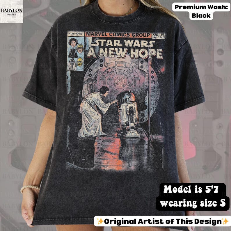 May include: Black t-shirt featuring a comic book-style graphic from Star Wars: A New Hope. The design includes Princess Leia and R2-D2. The shirt is a premium wash and the model is 5'7" wearing a size S.