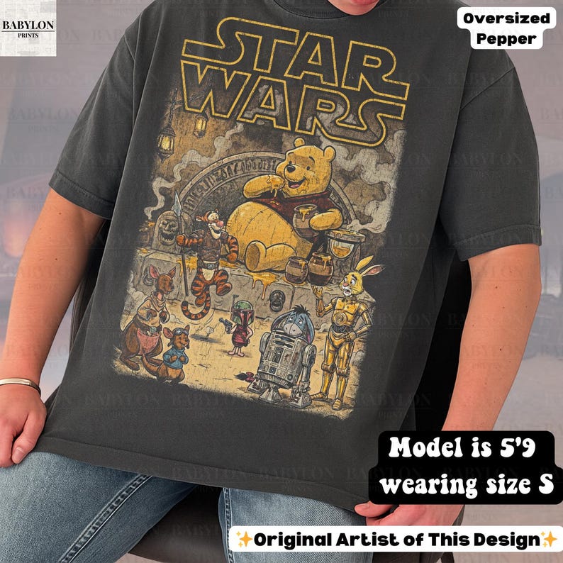 Może przedstawiać: Ciemnoszara, obszerna koszulka z grafiką Star Wars i Kubusia Puchatka. Projekt zawiera postacie takie jak Kubuś Puchatek, R2-D2 i inne. Tekst "STAR WARS" znajduje się na g&oacute;rze. Modelka ma 1,75 m wzrostu i nosi rozmiar S.