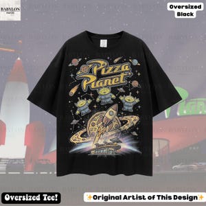 May include: Black oversized tee featuring a colorful Pizza Planet graphic. The design includes the text "Pizza Planet", aliens, a rocket ship, and a pizza planet. The shirt also has the text "Oversized Tee!" and "Original Artist of This Design".