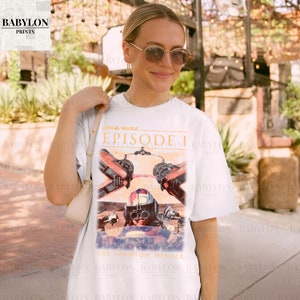 Op de afbeelding: Wit T-shirt met een Star Wars Episode I-afbeelding. Het ontwerp toont beelden uit "The Phantom Menace" met een piloot en ruimteschip. Het shirt heeft een ronde hals en korte mouwen, geschikt voor casual wear.