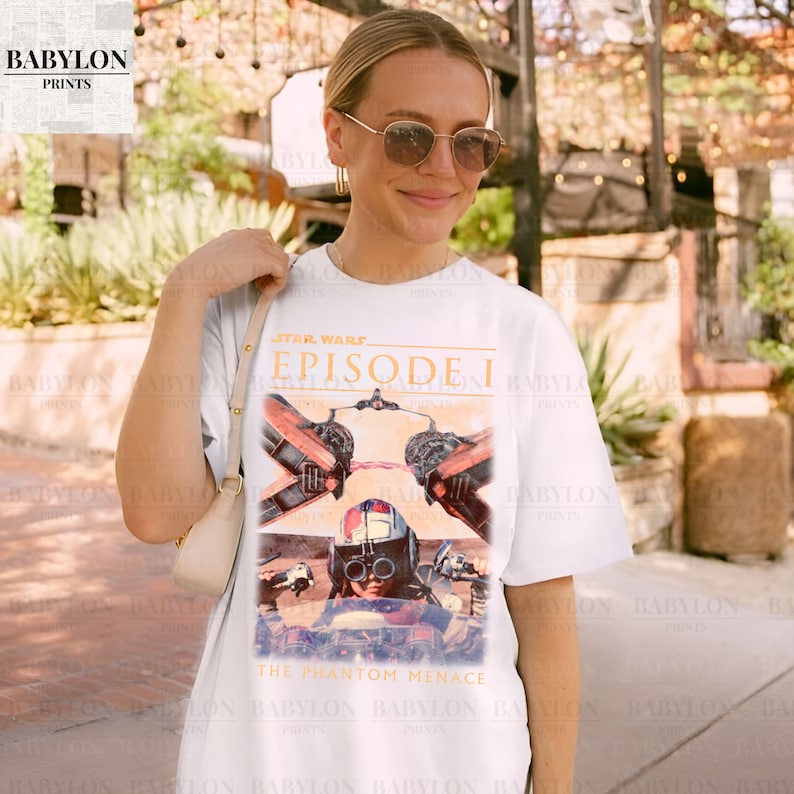 Op de afbeelding: Wit T-shirt met een Star Wars Episode I-afbeelding. Het ontwerp toont beelden uit "The Phantom Menace" met een piloot en ruimteschip. Het shirt heeft een ronde hals en korte mouwen, geschikt voor casual wear.