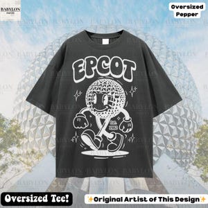 Pu&ograve; includere: T-shirt oversize grigio scuro con la scritta "EPCOT" sopra un personaggio dei cartoni animati di una sfera geodetica sorridente. Il personaggio cammina con un bastone e la scritta "Est. 1982" &egrave; sotto. La maglietta ha il testo "Oversized Tee!" e "Original Artist of This Design" in basso.