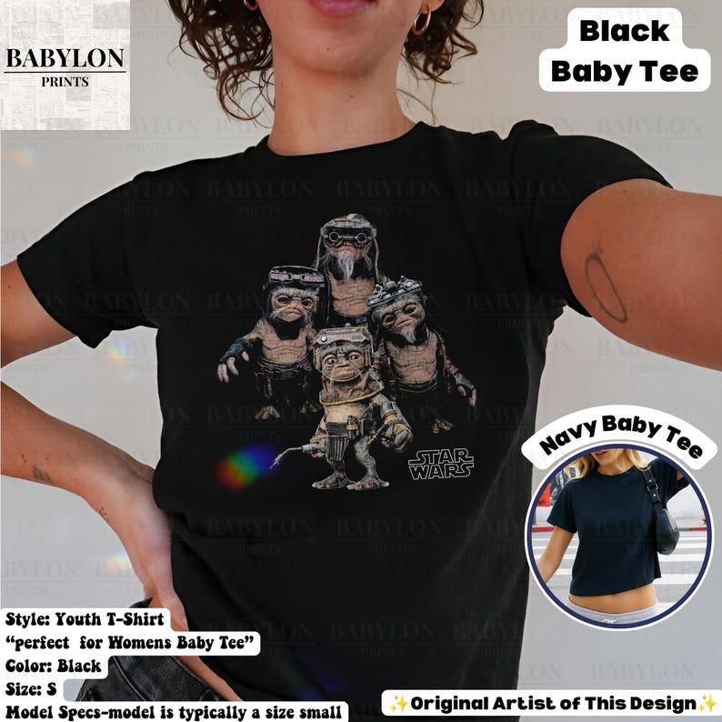 Op de afbeelding: Een zwart t-shirt met korte mouwen en een grafische print van vier kleine, harige wezens met een bril en een regenboogkleurig lichteffect. De tekst "STAR WARS" staat in het wit rechtsonder de afbeelding. Een kleine cirkelvormige inzet toont een marineblauwe versie van het t-shirt.