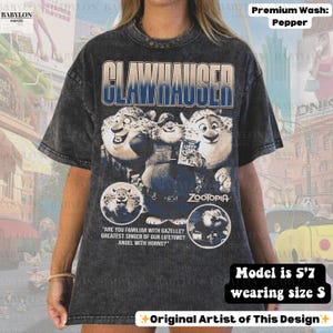 May include: Dark gray t-shirt featuring the word "CLAWHAUSER" in blue, with a graphic of characters from the movie "Zootopia." The shirt includes text from the movie and is a premium wash in pepper color.