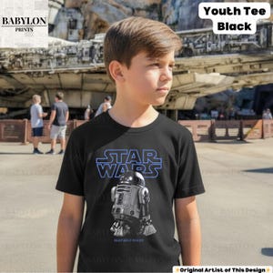 K&ouml;nnte beinhalten: Schwarzes Kinder-T-Shirt mit dem Star Wars-Logo in Blau und einer R2-D2-Grafik. Das Shirt hat den Text "BEEP BEEP WOOO!". Das Babylon Prints-Logo befindet sich oben links. Die Worte "Youth Tee Black" stehen oben rechts.