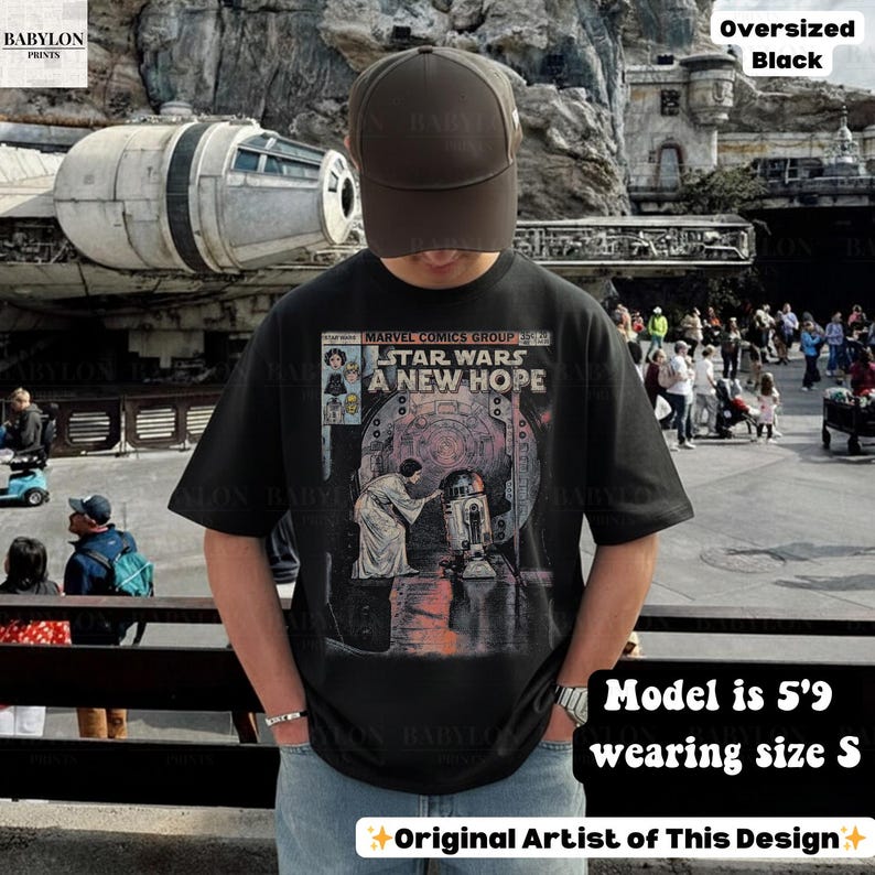May include: Black oversized t-shirt featuring a comic book-style graphic from Star Wars: A New Hope. The shirt has short sleeves and is worn with a brown baseball cap. The text "STAR WARS A NEW HOPE" is visible on the front.
