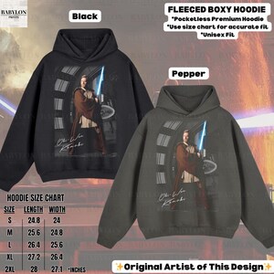 Może przedstawiać: Czarne i pieprzowe bluzy z kapturem z polaru z grafiką postaci trzymającej miecz świetlny. Bluzy mają napis "Obi-Wan Kenobi" i tabelę rozmiar&oacute;w. Bluzy są unisex i bez kieszeni.
