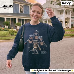 Op de afbeelding: Een marineblauw sweatshirt met lange mouwen en een grafische print van vier Ewok-personages uit Star Wars. Het ontwerp bevat het Star Wars-logo in witte tekst. Het sweatshirt heeft een ronde hals en geribbelde boorden bij de mouwen en zoom.