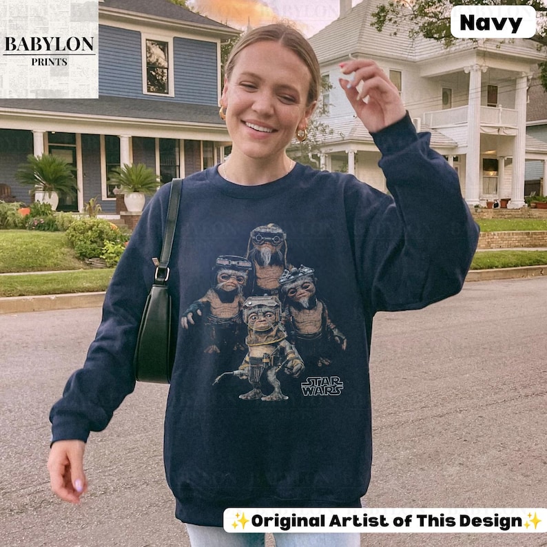 Op de afbeelding: Een marineblauw sweatshirt met lange mouwen en een grafische print van vier Ewok-personages uit Star Wars. Het ontwerp bevat het Star Wars-logo in witte tekst. Het sweatshirt heeft een ronde hals en geribbelde boorden bij de mouwen en zoom.