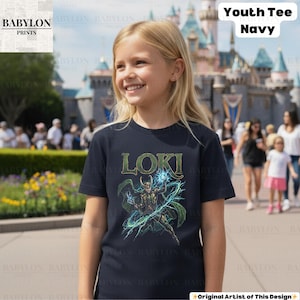 May include: A navy blue youth tee featuring the word "LOKI" in green lettering above a graphic of the character. The design includes a figure with a horned helmet, green cape, and blue energy effects. The shirt is worn by a young person.
