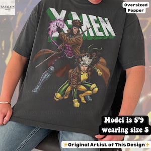 May include: Dark grey oversized t-shirt featuring a graphic of X-Men characters Gambit and Rogue. The word "X-MEN" is printed across the top in white and green. The shirt is a size S and the model is 5'9.