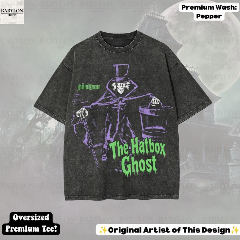 Puede incluir: Una camiseta oversize gris carb&oacute;n con lavado vintage. El frente presenta un gr&aacute;fico morado de The Hatbox Ghost de The Haunted Mansion, sosteniendo una sombrerera y un bast&oacute;n. El texto dice The Haunted Mansion y The Hatbox Ghost en verde.
