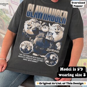 May include: Dark gray oversized t-shirt featuring a graphic of Clawhauser from the movie Zootopia. The design includes the text "CLAWHAUSER" and quotes. The shirt is a size S and the model is 5'9. Original artist design.