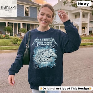 May include: Navy blue sweatshirt featuring a graphic of the Millennium Falcon spaceship with the text "Millennium Falcon" in a metallic font. The design includes blue lightning effects. The sweatshirt is a long-sleeved crew neck.