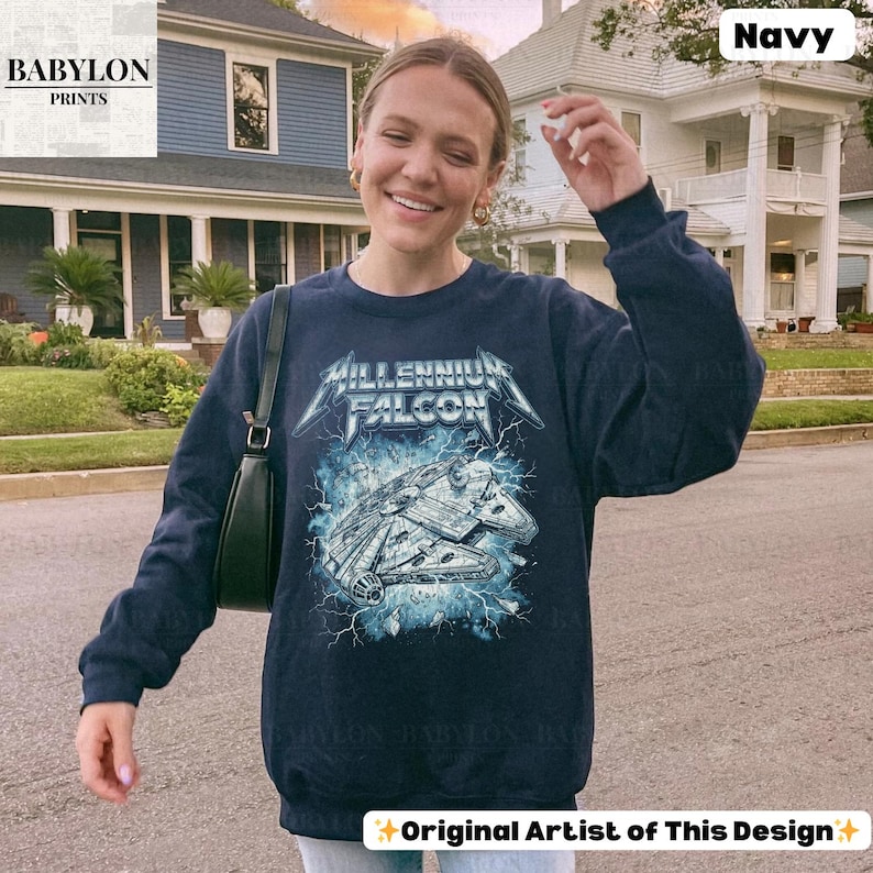 May include: Navy blue sweatshirt featuring a graphic of the Millennium Falcon spaceship with the text "Millennium Falcon" in a metallic font. The design includes blue lightning effects. The sweatshirt is a long-sleeved crew neck.