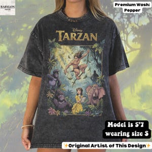 May include: A charcoal gray t-shirt featuring a colorful graphic from Disney's Tarzan. The design includes Tarzan, gorillas, Jane, and an elephant. The shirt has the text "Disney Tarzan" at the top. The shirt is a size S.