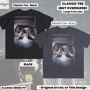 May include: Black and grey classic unisex fit t-shirts with a large print of a scene from a science fiction movie. The image features characters in a futuristic setting. Text on the shirts reads "Classic Tee" and "Original Artist of This Design."