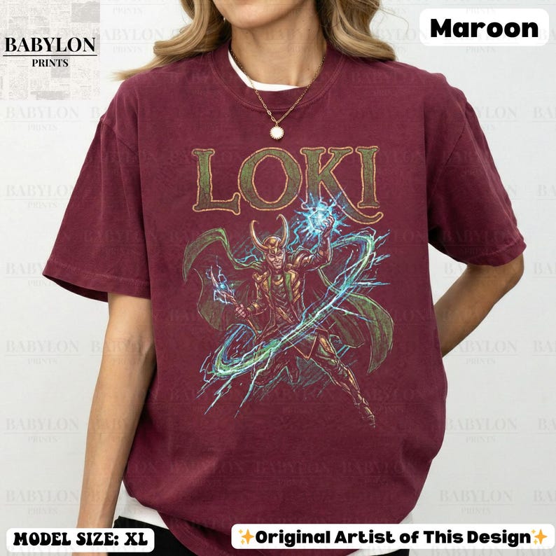 May include: Maroon t-shirt featuring the word "LOKI" in gold lettering above a detailed illustration of a character with a horned helmet, holding a glowing blue orb. The shirt is from Babylon Prints and the model is wearing size XL.