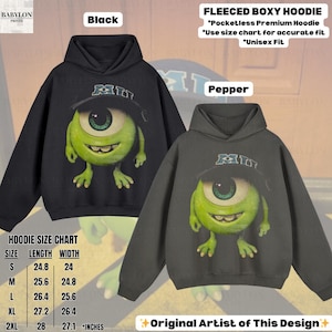 K&ouml;nnte beinhalten: Schwarze und pfefferfarbene Fleece-Boxy-Hoodies mit einer Cartoon-Figur mit einem Auge, die einen Hut tr&auml;gt. Die Hoodies haben den Text "MI" auf dem Hut. Das Bild enth&auml;lt eine Gr&ouml;&szlig;entabelle in Zoll und den Text "Original Artist of This Design".