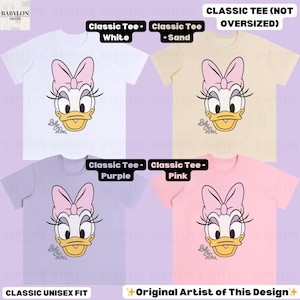 Puede incluir: Cuatro camisetas cl&aacute;sicas unisex en blanco, arena, morado y rosa. Cada camiseta presenta un gr&aacute;fico de Daisy Duck con un lazo rosa y pesta&ntilde;as. El texto en las camisetas dice "Classic Tee" y "Original Artist of This Design."