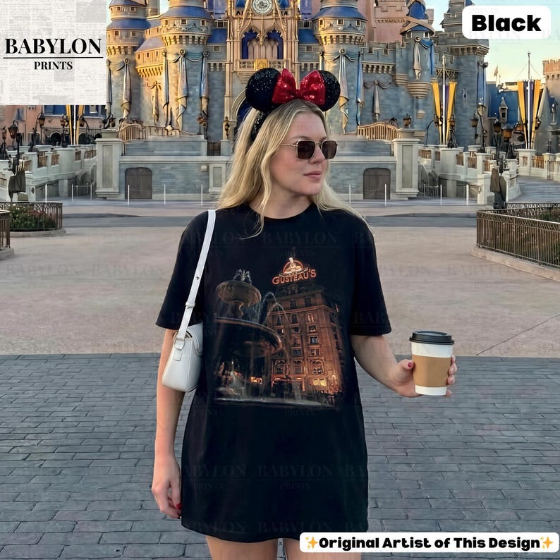 May include: Black t-shirt with a graphic of a building and the text "GUSTEAU'S". The shirt is from "BABYLON PRINTS". The person is wearing a black headband with mouse ears and a red bow, and sunglasses.