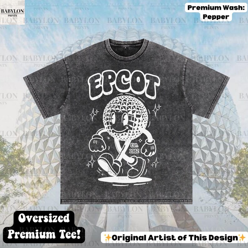 Pu&ograve; includere: T-shirt oversize grigio scuro con una grafica bianca di un personaggio a forma di globo sorridente e la scritta "EPCOT". Il design include il testo "Est. 1982". La maglietta ha il testo "Oversized Premium Tee!" e "Original Artist of This Design".