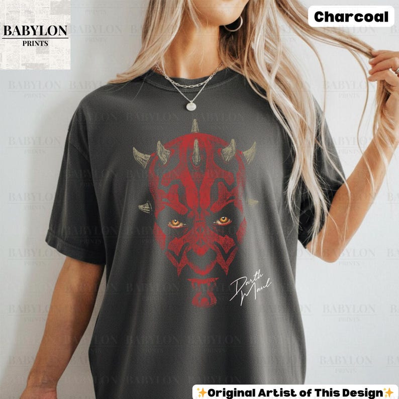 Może przedstawiać: Szary t-shirt z czerwonym nadrukiem twarzy Darth Maula z rogami i ż&oacute;łtymi oczami. Tekst "Darth Maul" jest napisany białym pismem poniżej. Logo Babylon Prints znajduje się w lewym g&oacute;rnym rogu.