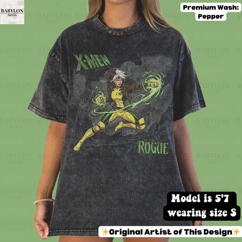 May include: A dark grey t-shirt with a graphic of the X-Men character Rogue in a yellow and green costume. The text "X-MEN" and "ROGUE" are printed on the shirt. The shirt is a premium wash, pepper colour.