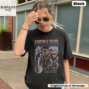 May include: Black t-shirt with a graphic print of Ahsoka Tano from Star Wars. The graphic features a collage of Ahsoka's face and a quote from the show: "I've learned that trusting others is not a weakness, but a strength."