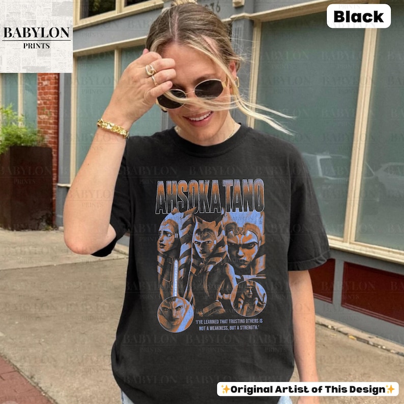 May include: Black t-shirt with a graphic print of Ahsoka Tano from Star Wars. The graphic features a collage of Ahsoka's face and a quote from the show: "I've learned that trusting others is not a weakness, but a strength."