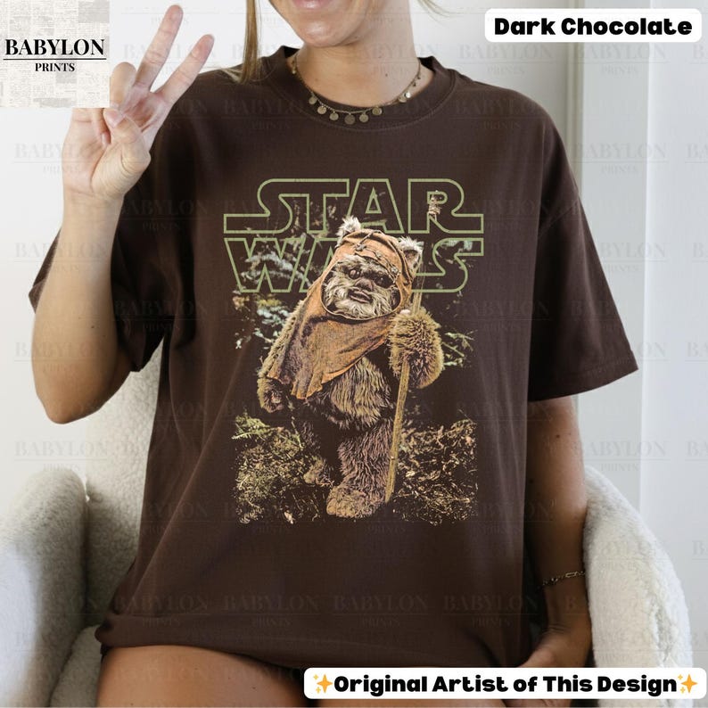 May include: Dark chocolate brown t-shirt featuring a Star Wars graphic. The design includes the Star Wars logo and an image of an Ewok character holding a staff. The shirt is from Babylon Prints.