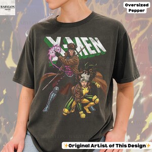 May include: Dark gray oversized t-shirt featuring the X-Men logo in green and white. The graphic includes illustrations of Gambit and Rogue. The shirt has the text "Oversized Pepper" and "Original Artist of This Design".