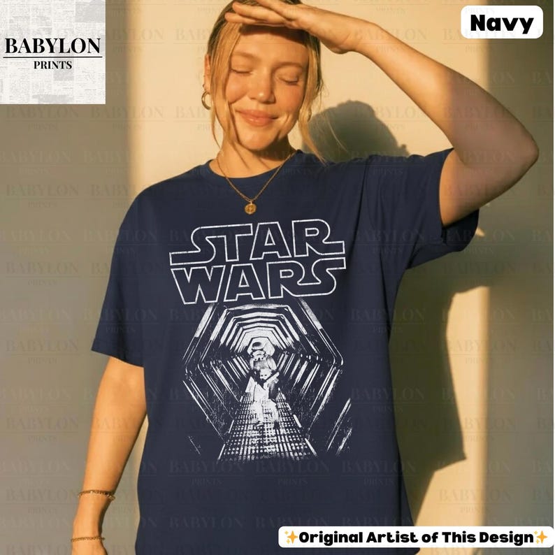 May include: Navy blue t-shirt featuring the Star Wars logo and a graphic of a Stormtrooper in a tunnel. The shirt has short sleeves and a crew neck. The text "Original Artist of This Design" is at the bottom.