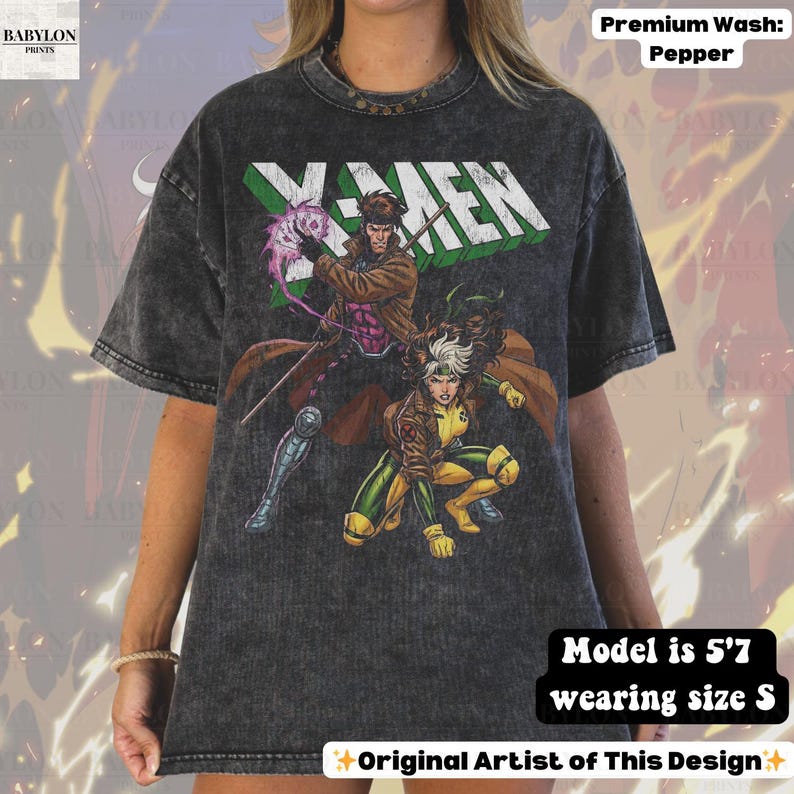 May include: A pepper-wash, charcoal-colored t-shirt featuring the X-Men logo in green and white. The graphic design includes illustrations of Gambit and Rogue. The model is 5'7" and wearing a size S. The design is by the original artist.