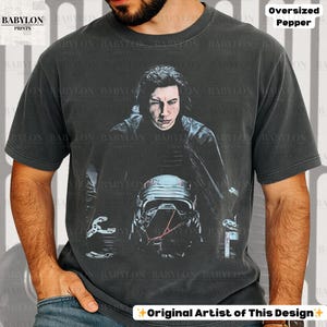 May include: Dark grey oversized t-shirt with a portrait of a person and a helmet. The shirt has the text "BABYLON PRINTS" and "Original Artist of This Design".